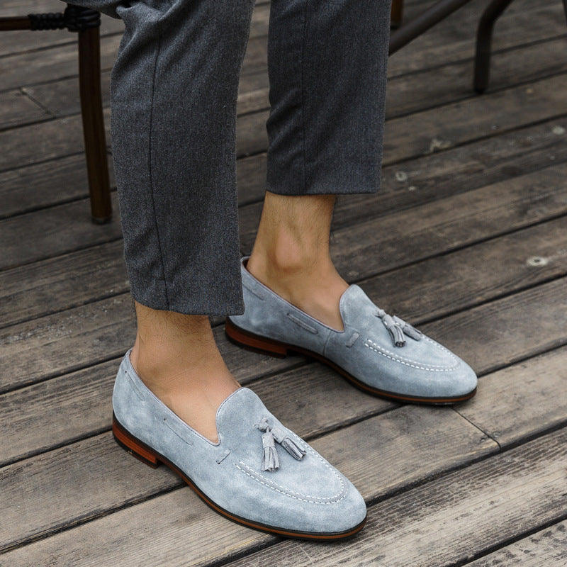 Light blue suede loafers with tassels worn on a wooden floor.