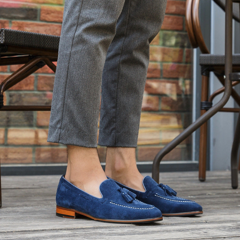 Person wearing blue loafers with tassels on a wooden floor.