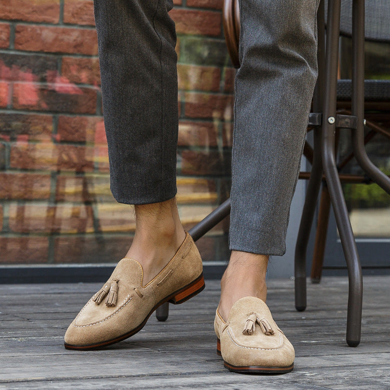 Beige loafers with tassels worn by a person on a wooden floor.