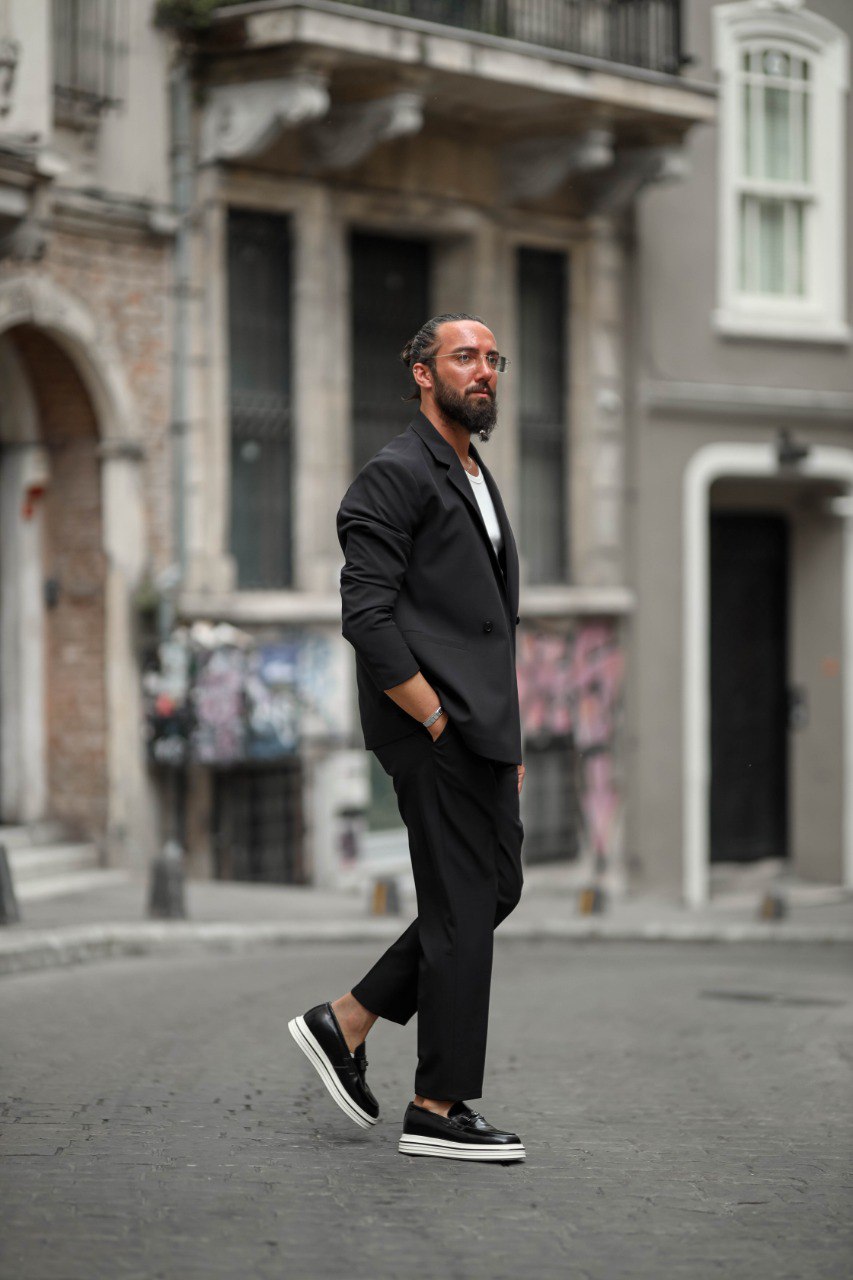 Man in a black suit walking on a city street with buildings in the background