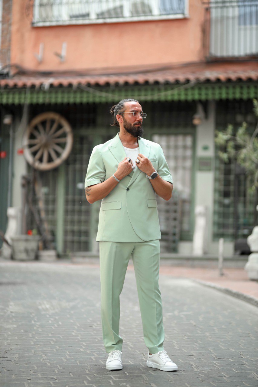 Man in a light green suit standing on a street with buildings in the background