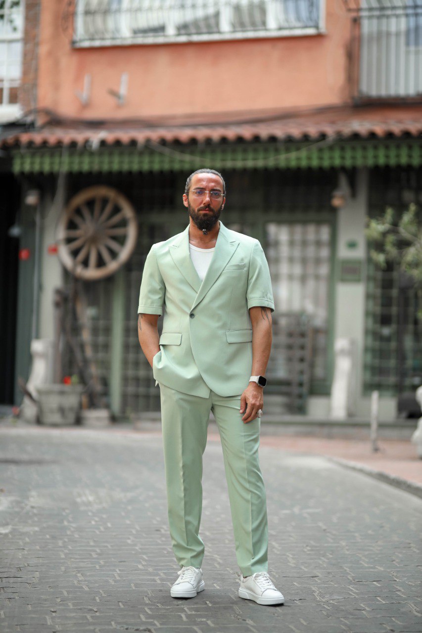 Man wearing a light green suit standing on a street with buildings in the background