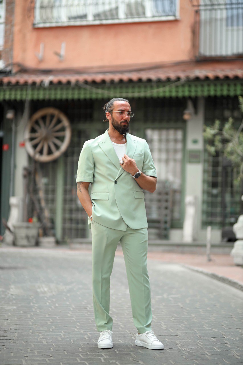 Man in a light green suit standing on a street with buildings in the background