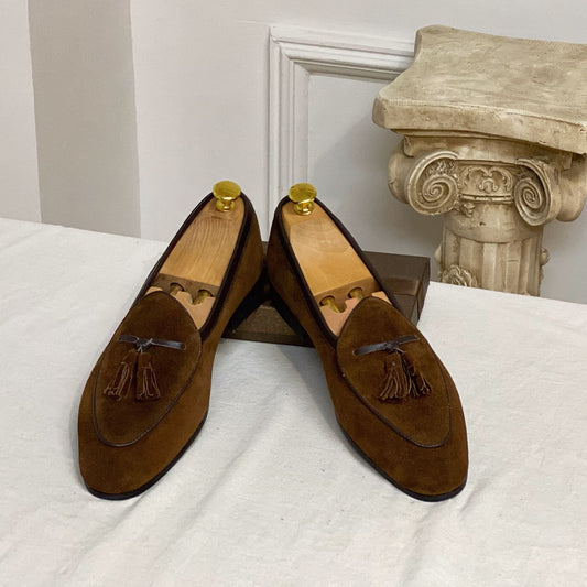 Pair of brown suede loafers with tassels on a white surface.