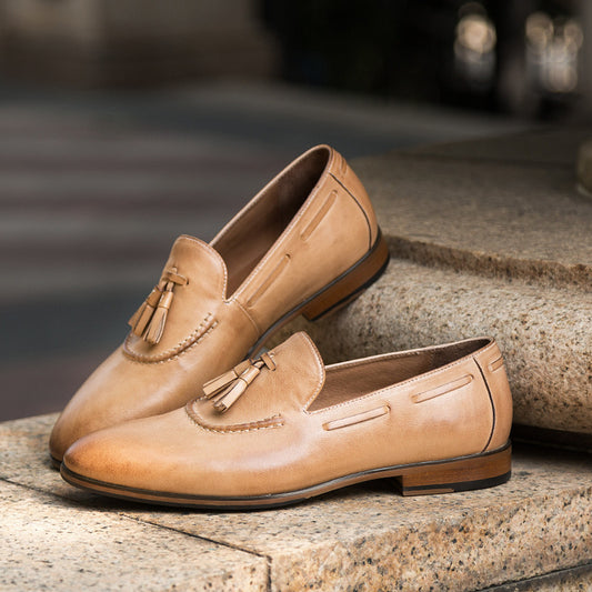 Pair of tan loafers with tassels on a stone surface