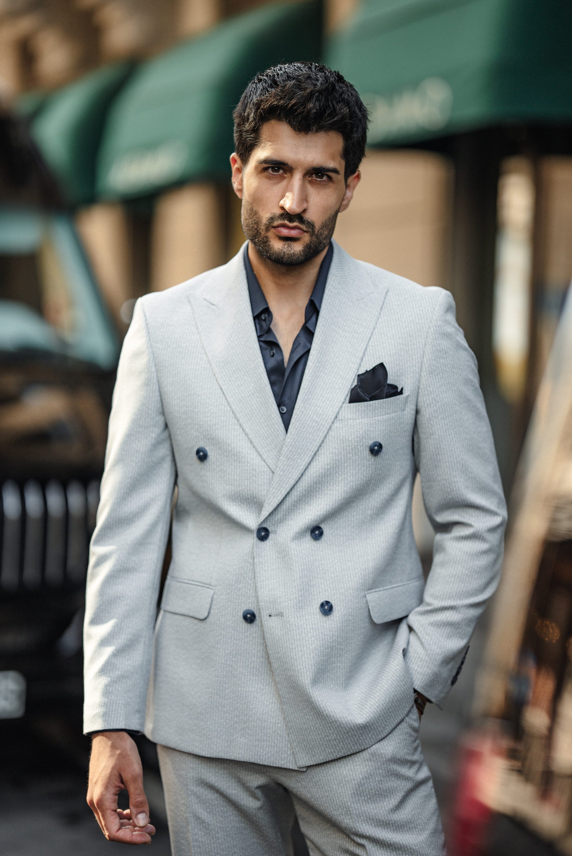 Man wearing a light gray suit with black buttons in an urban setting