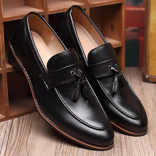 Pair of black leather loafers with tassels on a wooden floor.