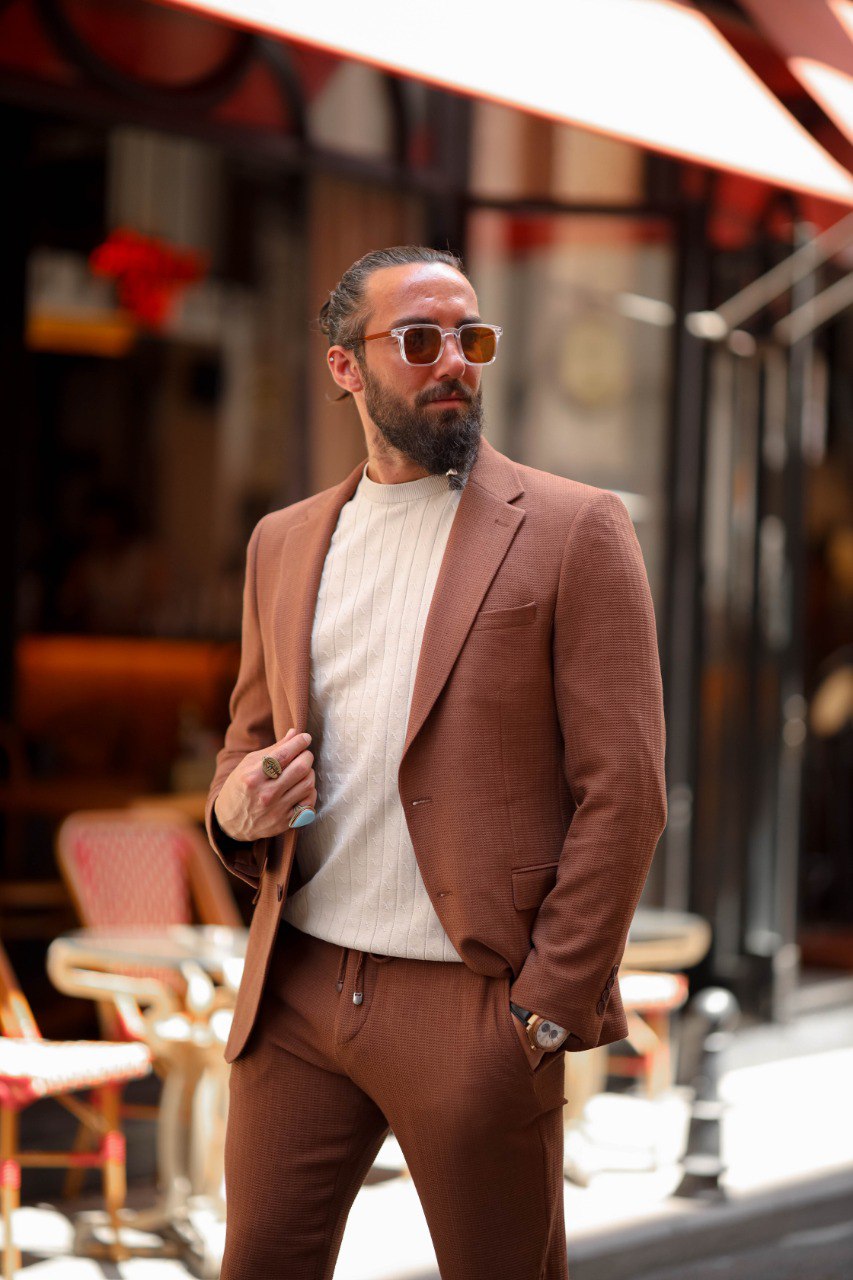 Man in a brown suit standing outdoors with blurred background
