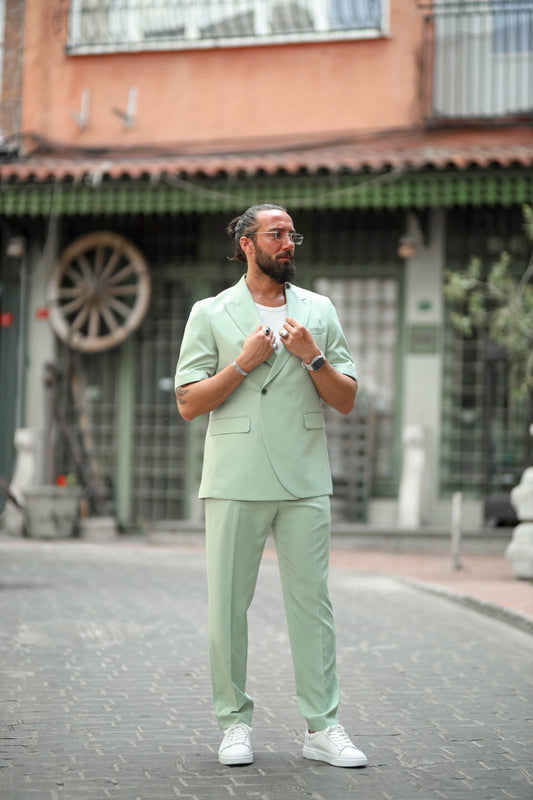 Man in a light green suit standing on a street with buildings in the background